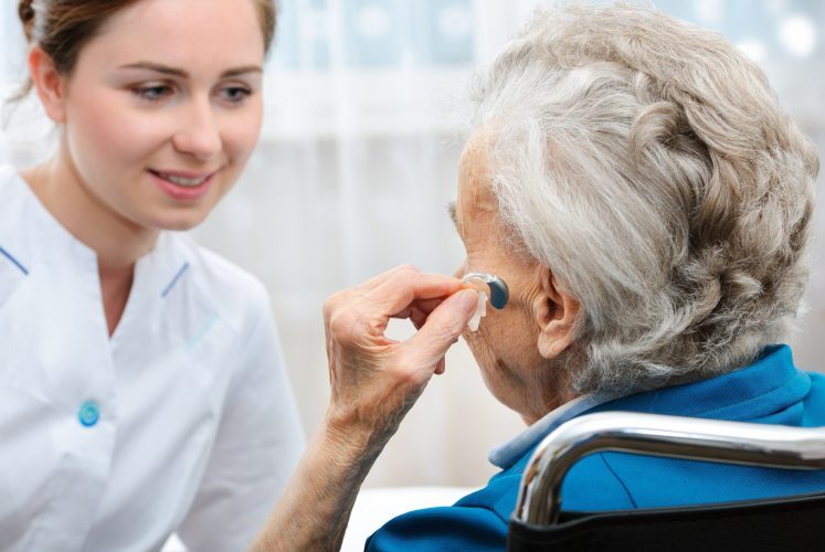 Older adult being fitted with a hearing aid.
