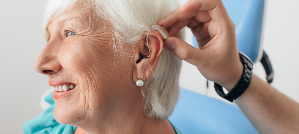 "Senior woman smiling as a healthcare professional adjusts her hearing aid."